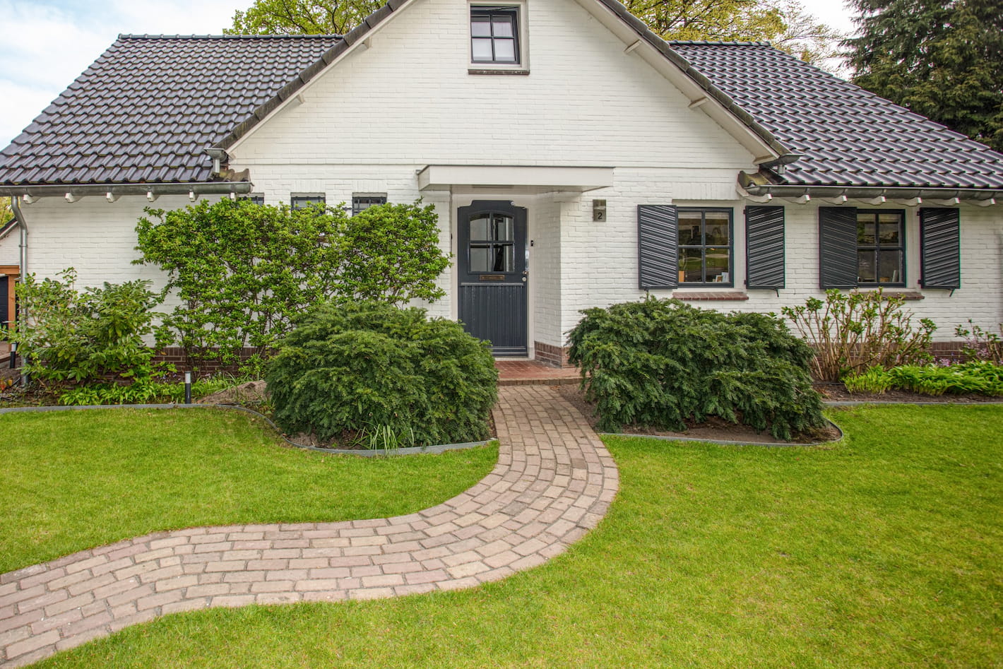 Voortuin van een huis met een kronkelend pad en groene struiken, onderdeel van een tuinrenovatie in Hilversum door Snijers Tuinen.