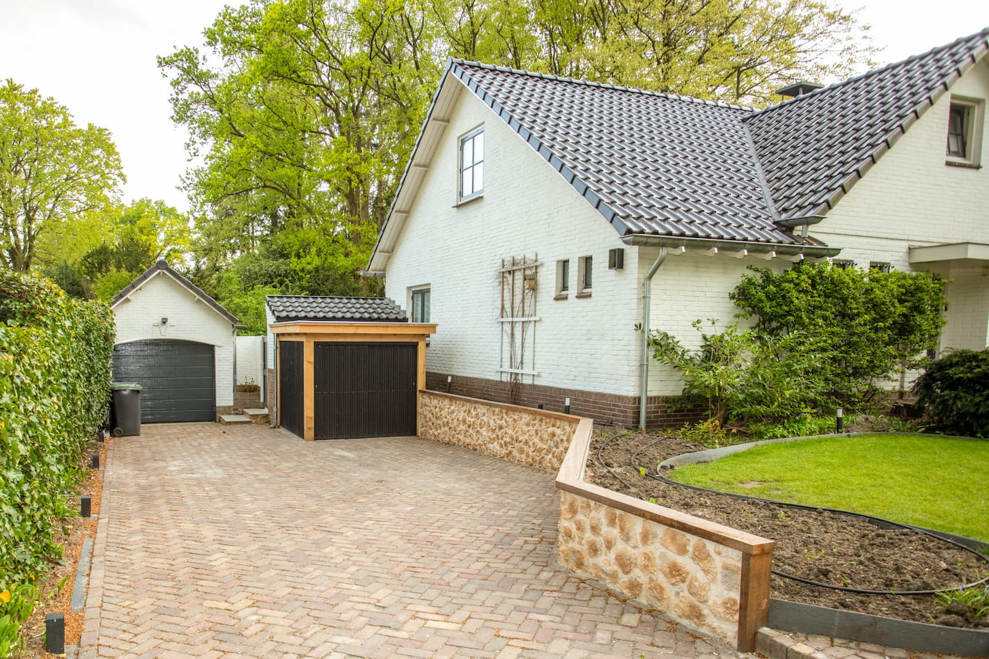 Oprit en garage van een huis met betegelde muur, bij een tuinrenovatie in Hilversum door Snijers Tuinen.