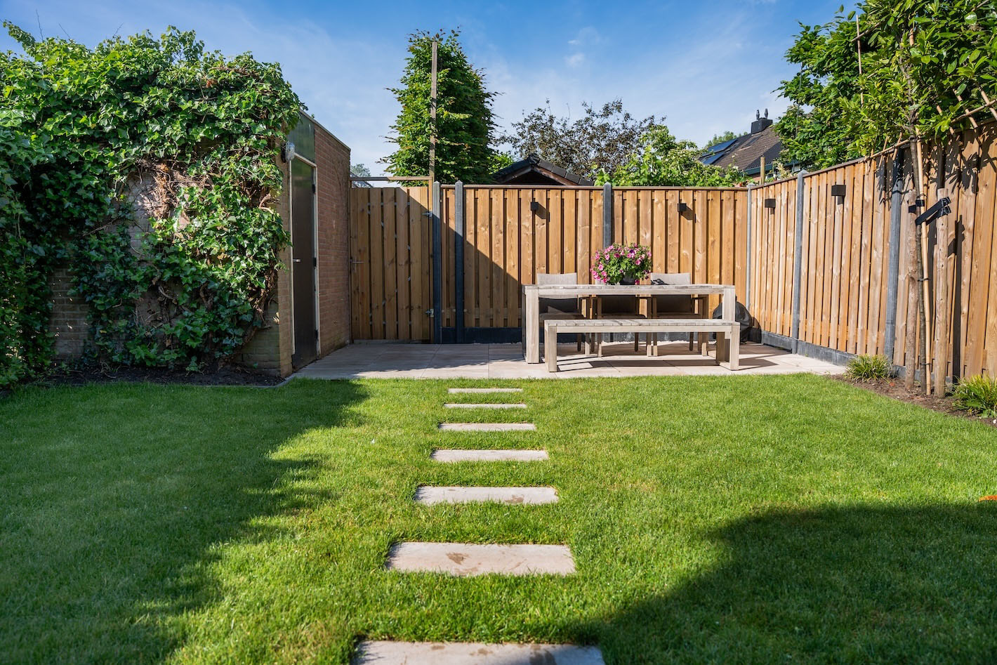 Moderne grijze tuinbanken bij de achtergevel van een gerenoveerd huis in Huizen door Snijers Tuinen.