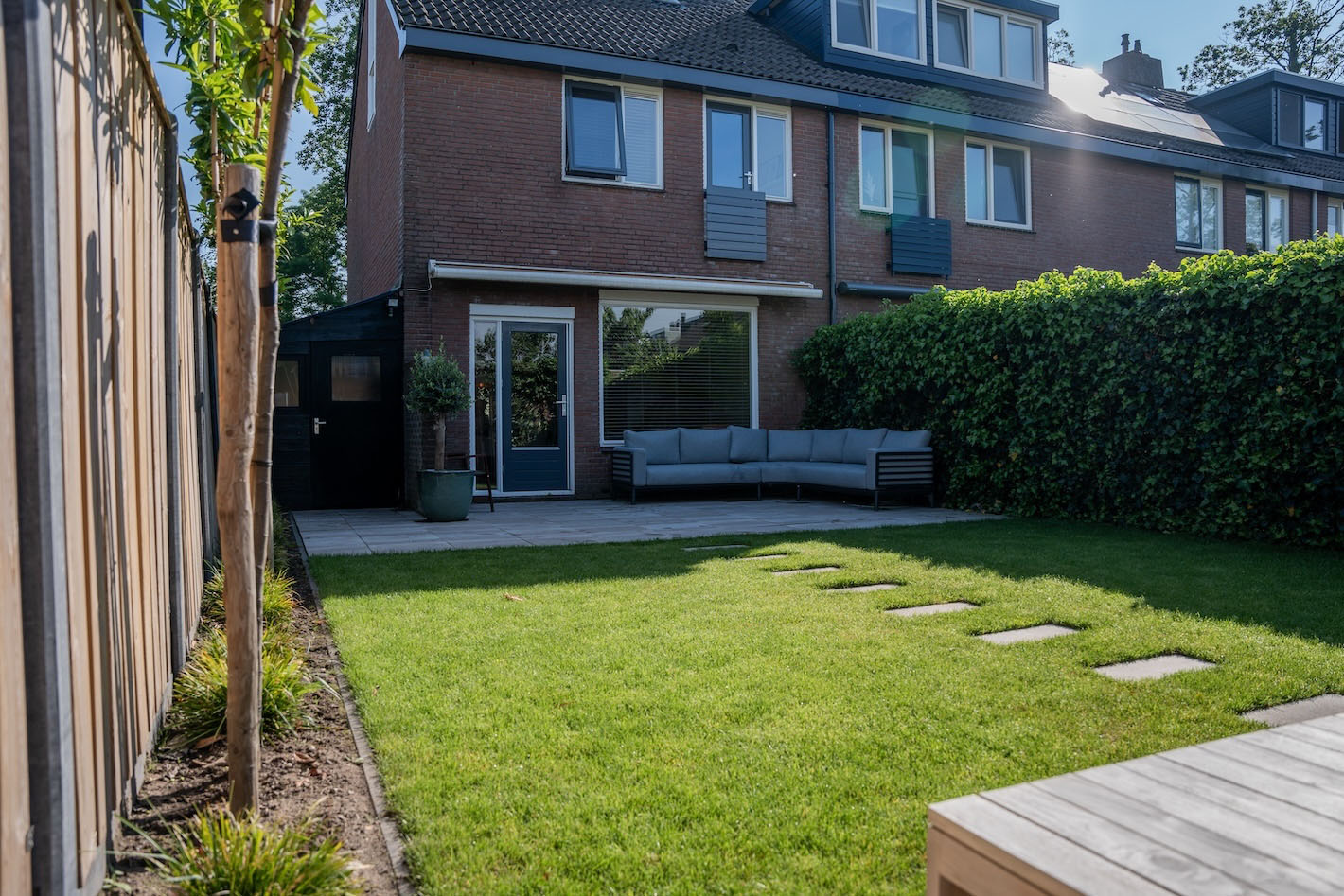 Achtertuin met houten schutting, betegeld terras en stapstenen in het gras bij tuinproject in Huizen door Snijers Tuinen."