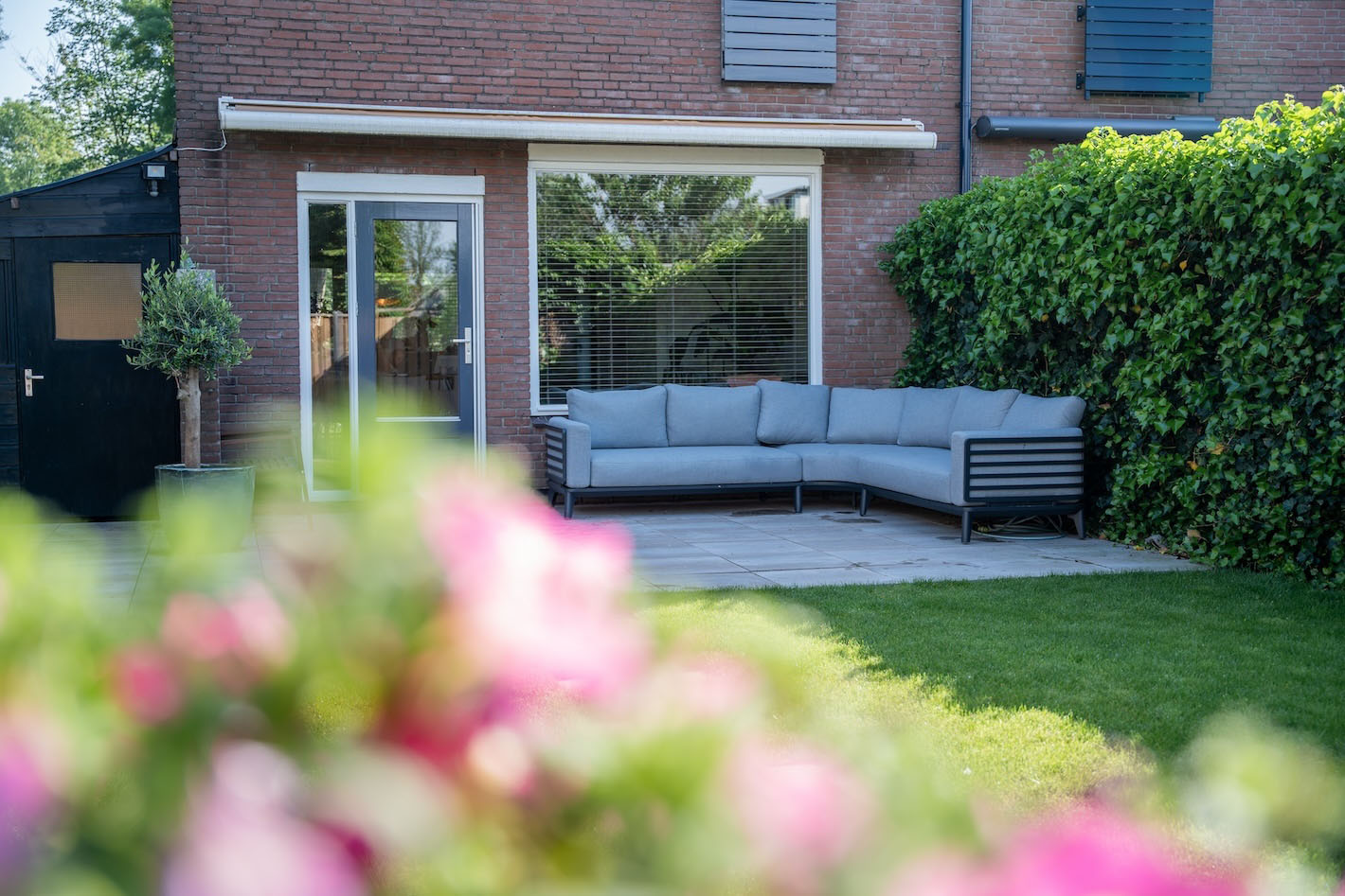 Achtertuin van gerenoveerd huis in Huizen door Snijers Tuinen met gazon, houten schutting, en betegeld terras.