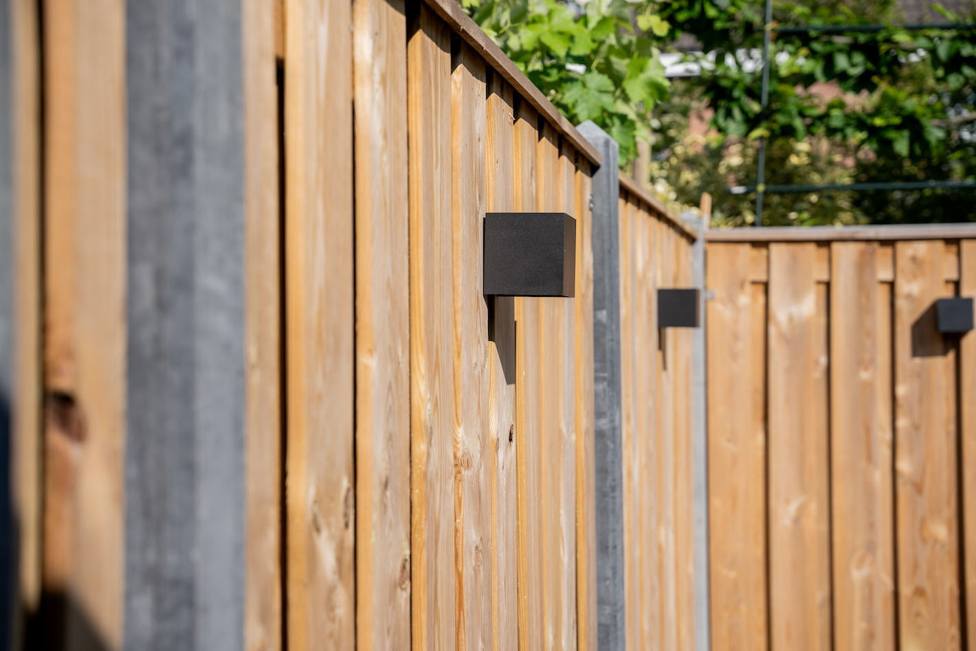 Houten schutting met zwarte wandlampen bij tuinproject in Huizen door Snijers Tuinen."